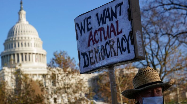 Protester David Barrows carries a sign during a rally to press Congress to pass voting rights protections and the "Build Back Better Act," Monday, Dec. 13, 2021, in Washington. A new poll finds that only about 1 in 10 U.S. adults give high ratings to the way democracy is working in the United States or how well it represents the interests of most Americans. (AP Photo/Patrick Semansky, File)