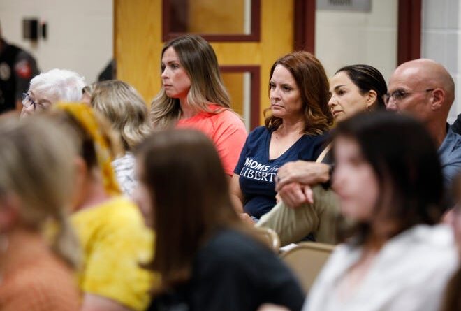 A woman (back row, second from left) wears a blue Moms for Liberty T-shirt at the June 20 Nixa school board meeting.  Pictured at right are Springfield School Board member Maryam Mohammadkhani and retired police officer David Nokes, who ran for the Springfield City Council in April.